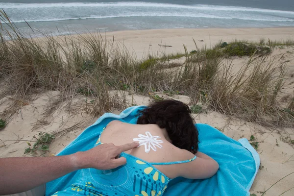 Hand of man putting on woman suntan lotion at beach