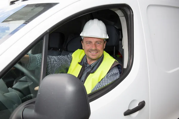 Construction worker driving a car. He is wearing a white helmet