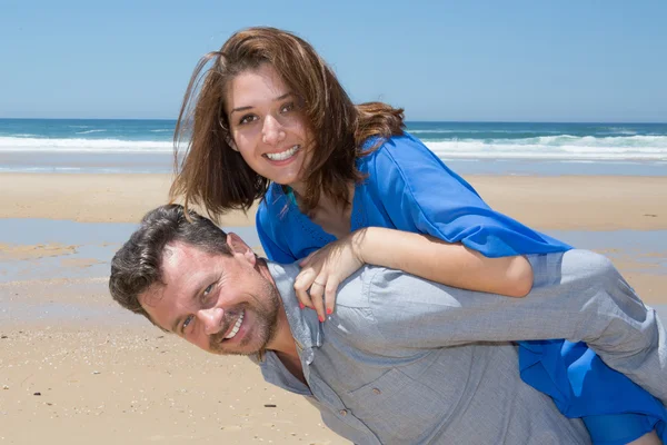 Happy couple smiling at the beach man giving piggyback