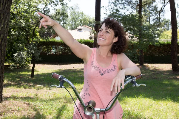 Middle aged woman leaning on bike pointing her finger