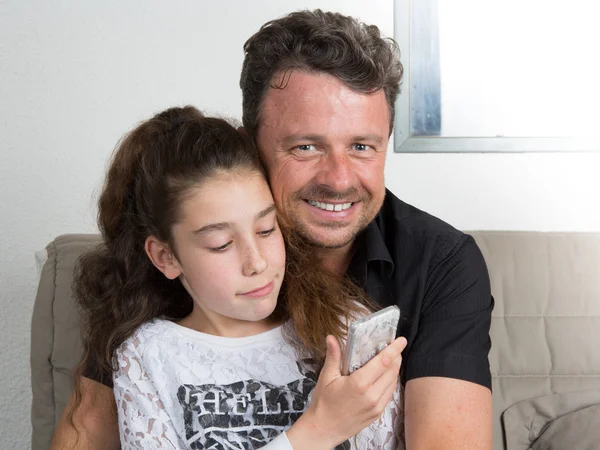 Smiling father and his brunette daughter using cell phone