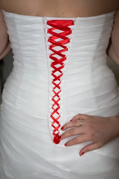 Bridesmaid tie the red laces on the back of a wedding dress closeup