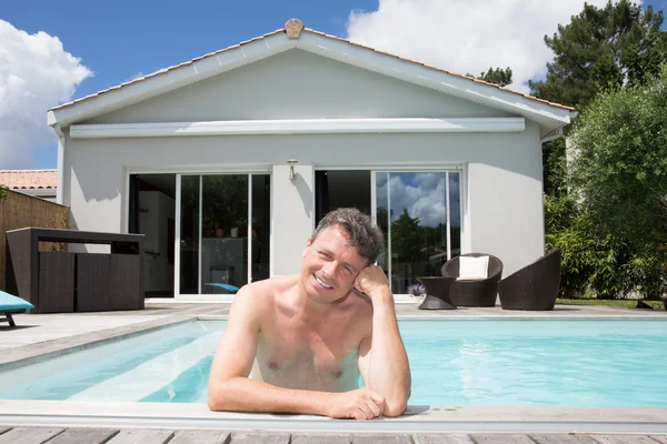 Happy man in private swimming pool in front of his house