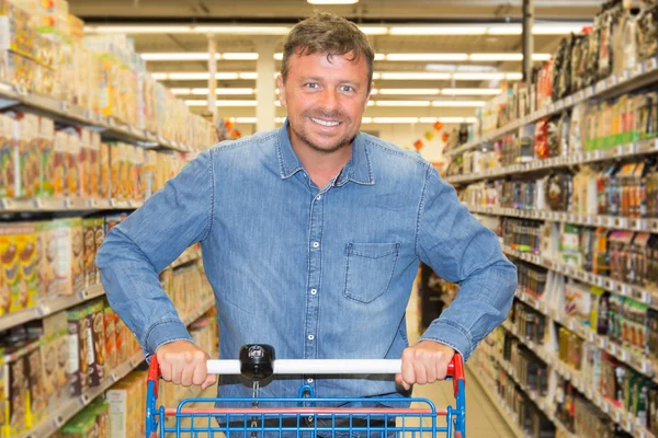 Confident man driving shopping cart while grocery shopping in supermarket