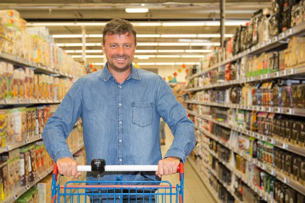 Smiling man driving shopping cart while grocery shopping in supermarket
