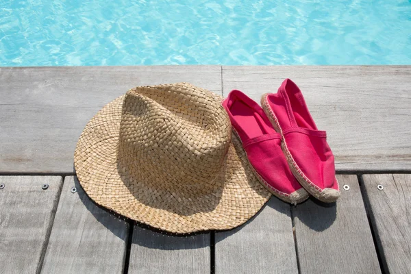 Summer background with hat shoes on the wooden deck and pool