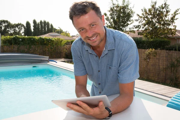 Happy man standing by the pool smiling with digital tablet