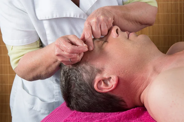 Acupuncturist prepares to tap needle around face of man