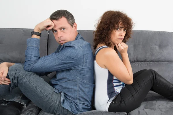 Man and woman unhappy and sad sitting back to back on sofa at home