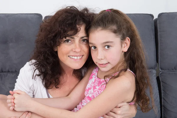 Brunette curly hair mother and long hair daughter on couch