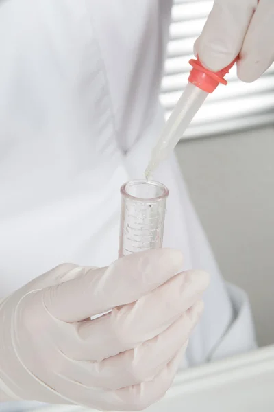 Science, chemistry, technology, biology and people concept - close up of scientists hands with pipette filling test tube making research in clinical laboratory