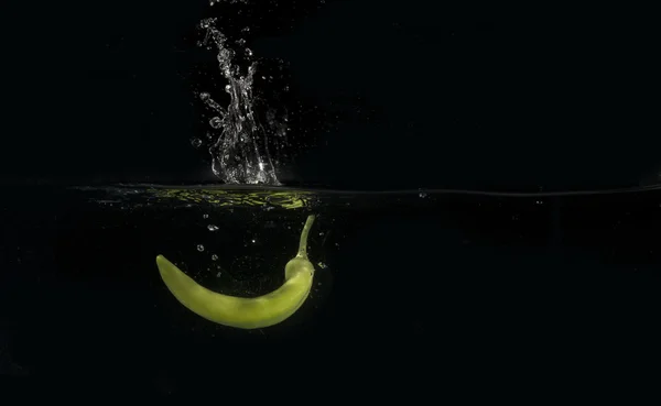 Green Banana pepper Splashing Into Water On Black