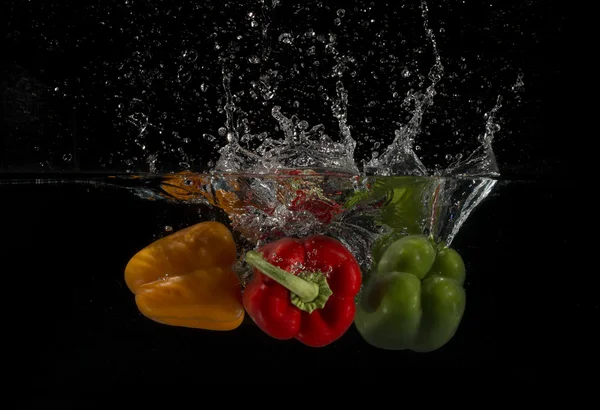 Three Peppers Splashing Into Water On Black