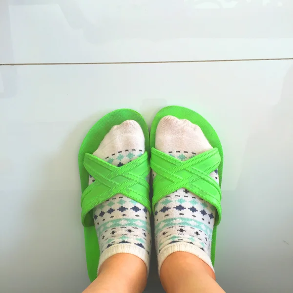 Selfie feet wearing white polka dot socks and green flip-flops on white floor background
