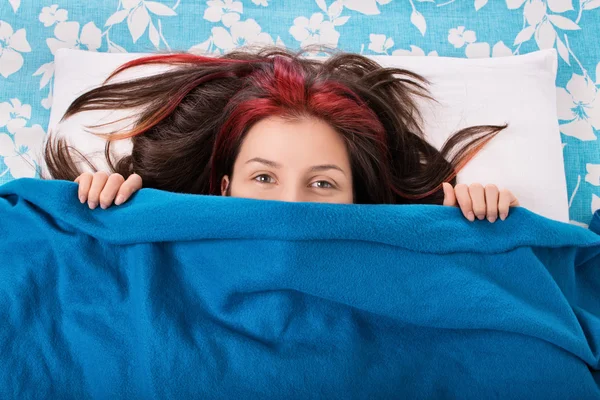 Young girl hiding behind a blanket on her bed