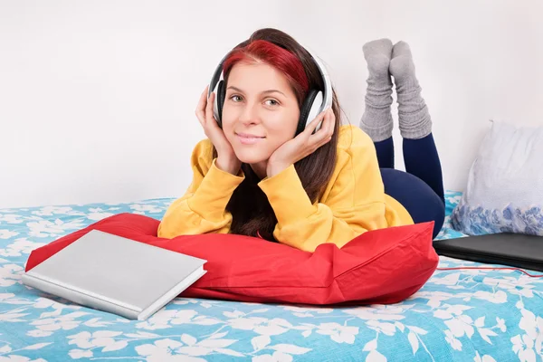 Girl in bed with headphones, book and a laptop