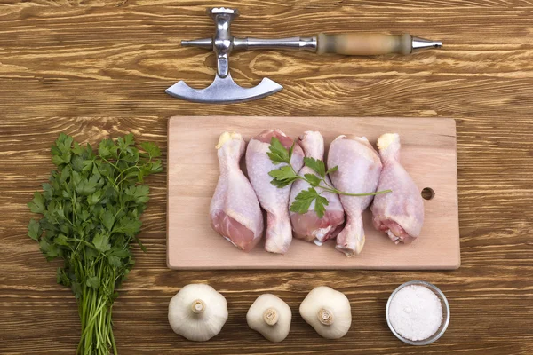 Raw chicken drumstick on board with salt, garlic, parsley, ax