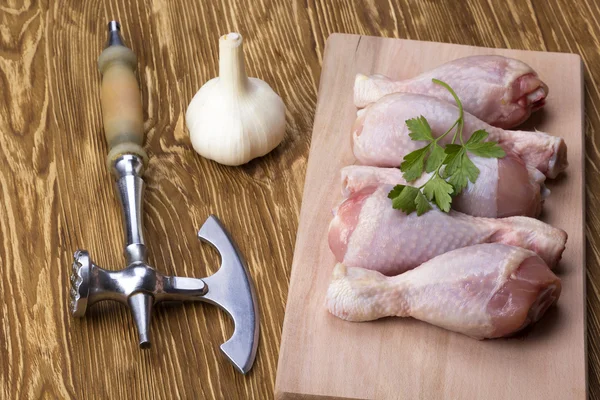 Raw chicken drumstick on board with garlic and ax