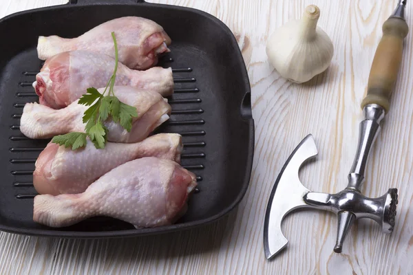 Raw chicken drumstick on pan with garlic and ax
