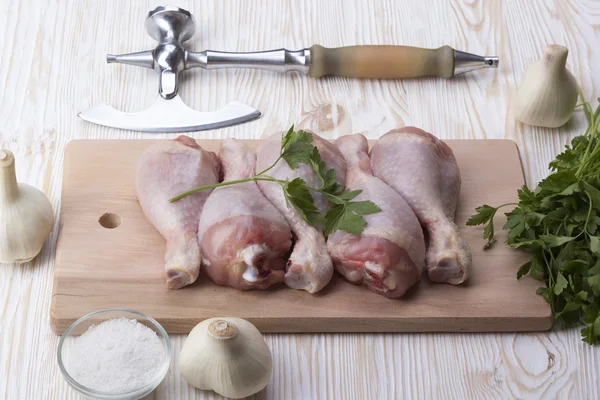 Chicken drumstick on board with salt, parsley, garlic and ax