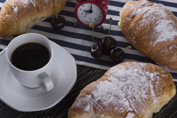 Alarm clock and breakfast with cherry, coffee , croissant.