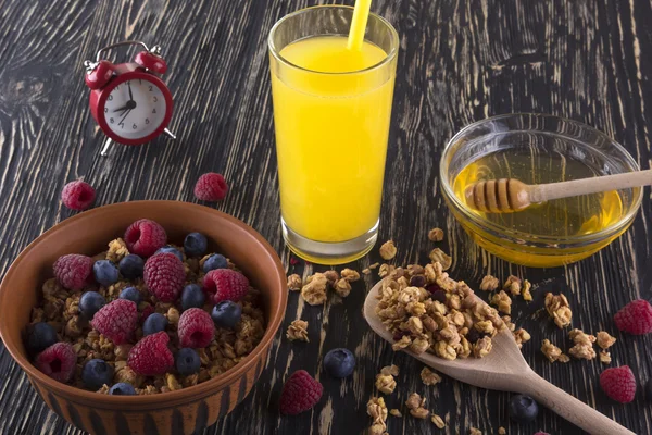 Muesli with fresh berries, orange juice, honey and alarm clock.