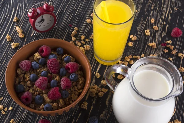 Muesli with fresh berries, orange juice, milk and alarm clock.