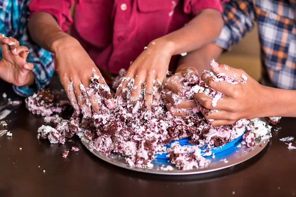 Three childrens hands smash cake.