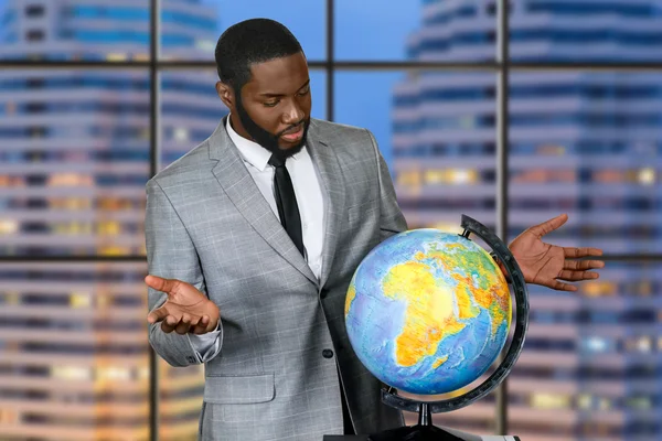 Puzzled afro businessman beside globe.
