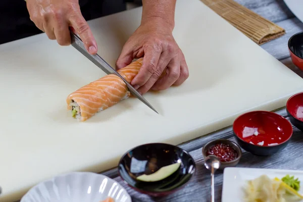 Hand holding knife cuts sushi.