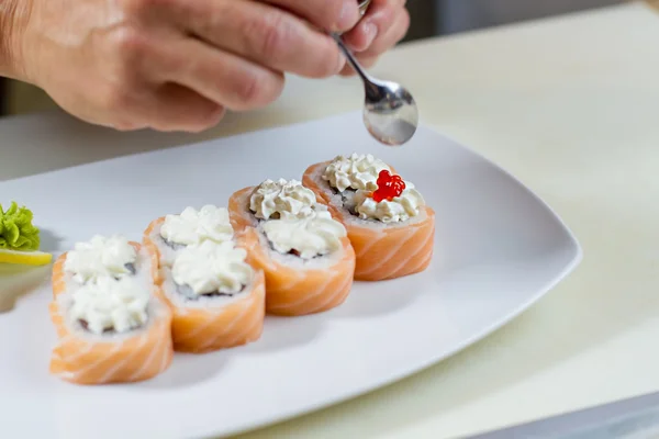 Hand holds spoon over sushi.