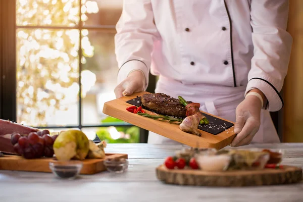 Cook holds board with meat.