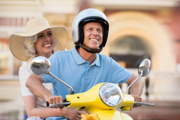 Mature couple on scooter smiles.