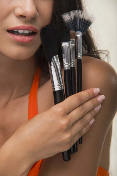 Girl in orange shirt is showing cosmetic brushes.