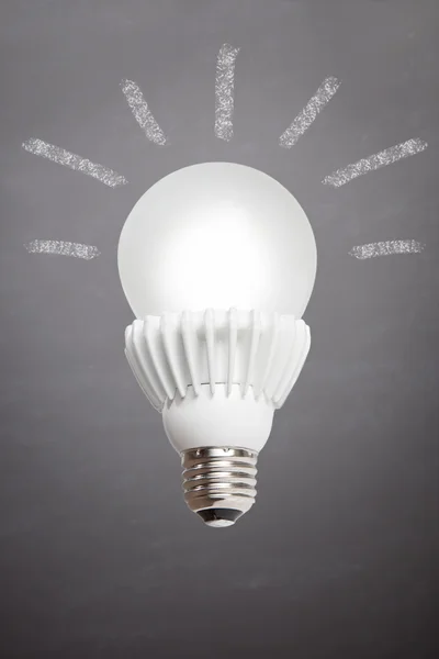 Glowing LED bulb on chalkboard background with rays