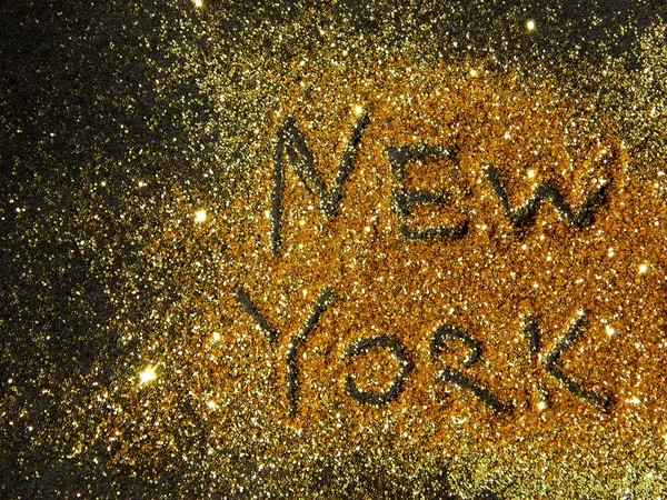 Blurry inscription New York on golden glitter sparkle on black background