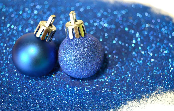 Two blue Christmas balls on blue glitter on white background