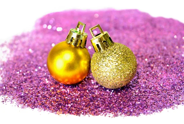 Two golden Christmas balls on purple glitter on white background