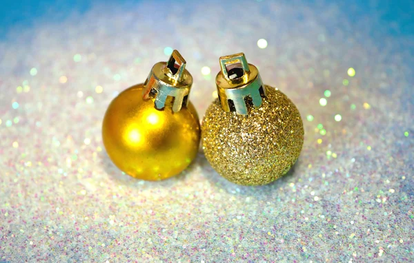 Two golden Christmas balls on white glitter on blue background