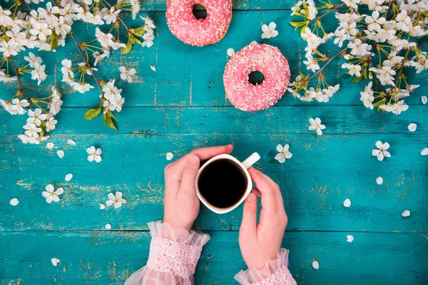 The concept with morning coffee in a romantic style on the wooden background. Cherry blossoms, donuts, smartphone, coffee and hand in the frame.