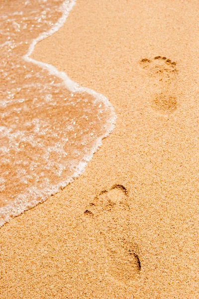 Footprints in the sand  with sea wave vertical