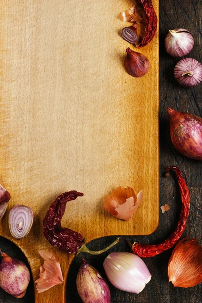 Wooden board with onions, garlic and pepper background