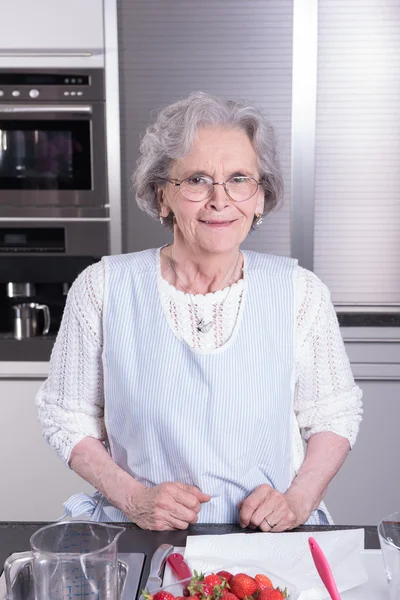 Active female pensioner is preparing strawberries in the kitchen