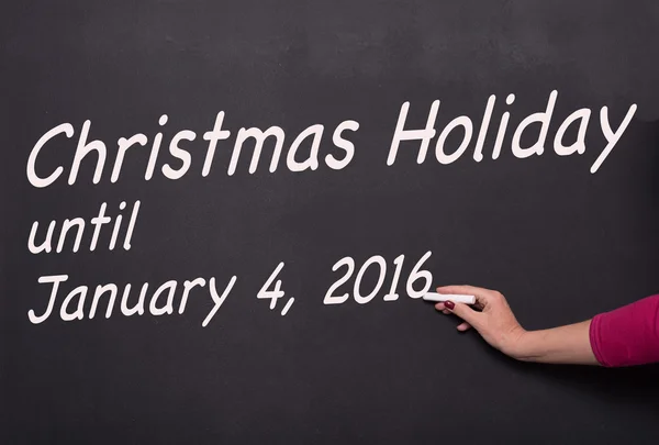 Woman's hand with chalk on blackboard writing christmas holiday