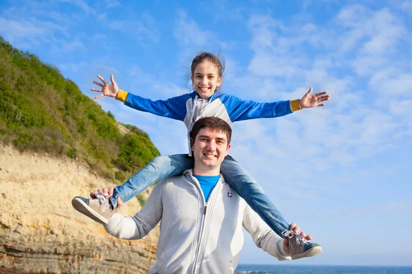 Girl sitting on dad\'s shoulders on sea background