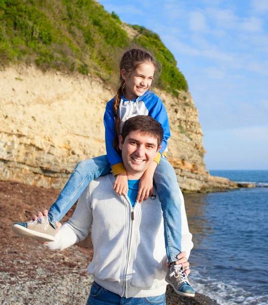 Girl sitting on dad\'s shoulders on sea background