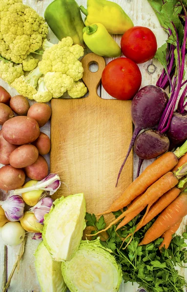 Food frame, market fresh food. Assorted organic vegetables and spices for healthy cooking and lifestyle on rustic wooden background with wooden cutting board in middle and copy space for text