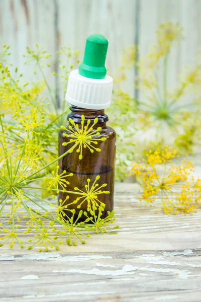 A dropper bottle of dill essential oil. Fresh dill leaves in the background