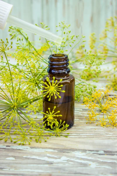 A dropper bottle of dill essential oil. Fresh dill leaves in the background