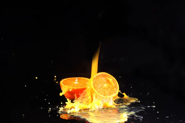 The orange on a black background, orange juice flows on oranges